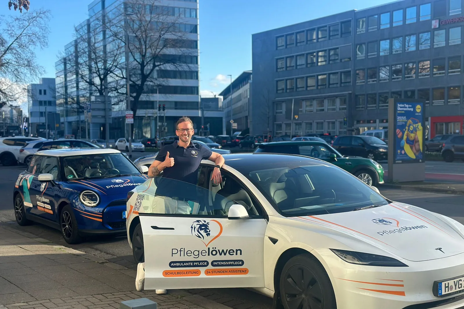 Björn Hartmann am Pflegelöwen-E-Auto mit der Aufschrift „24 Stunden Assistenz“
